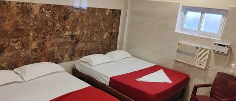 A hotel room with two beds, a red chair, a ceiling fan, and a window with a view.