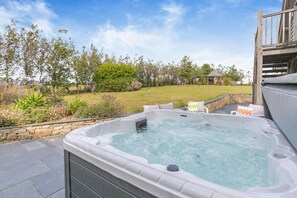 A hot tub with a stone wall and a grassy yard in the background. - 4 Bed in Instow (oc-h32283) (Westleigh)