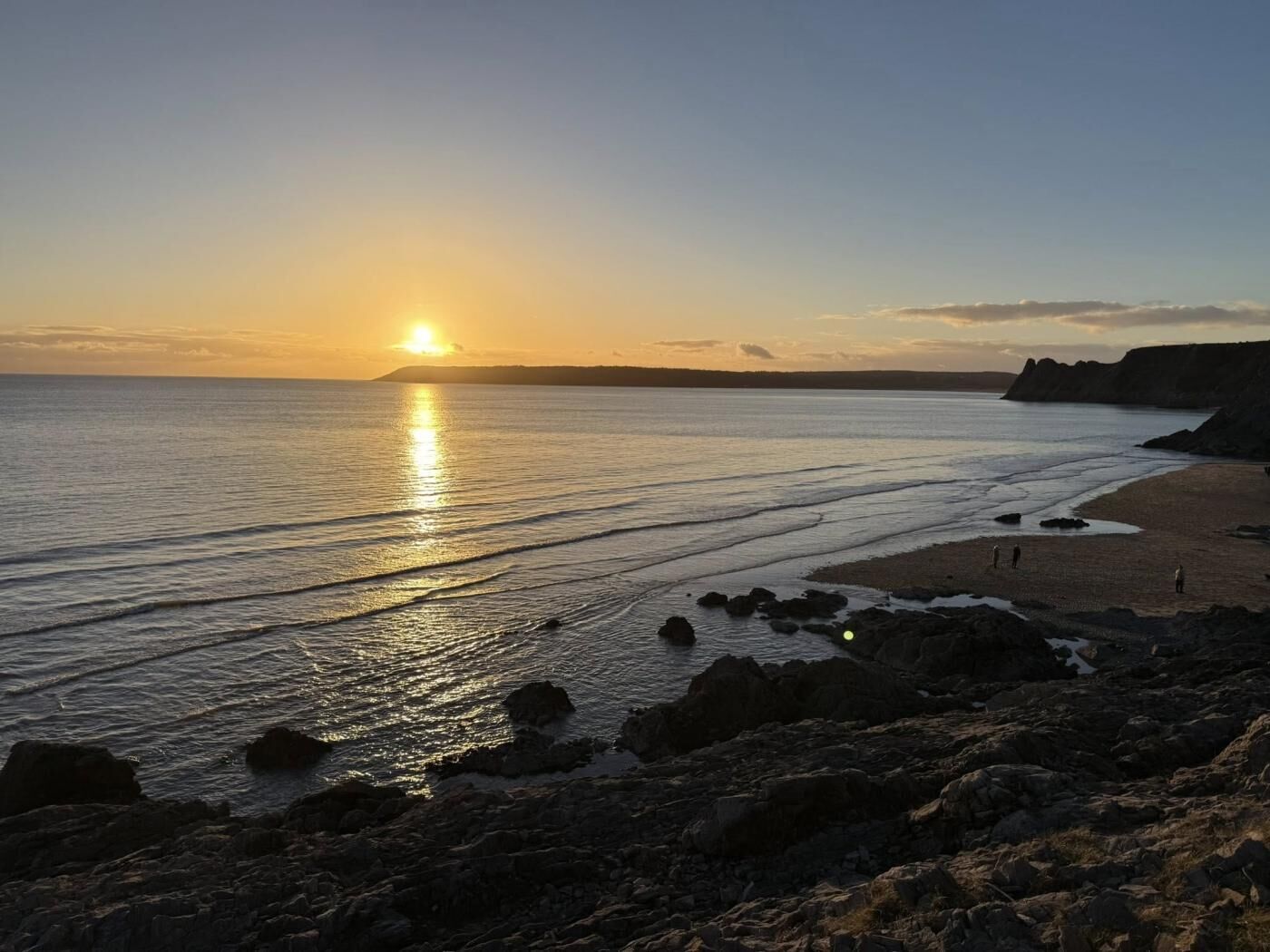 A coastal sunset with a beach and rocky foreground.