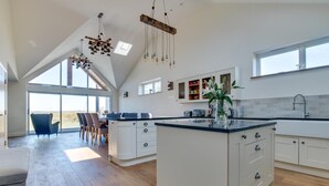 A spacious kitchen with a large island, modern pendant lights, and a view through large windows. - 4 Bed in Pennard (oc-hh390) (Southgate)