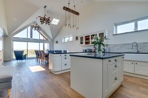 Une cuisine spacieuse dotée d’un grand îlot central, de luminaires suspendus modernes et offrant une vue dégagée grâce à de grandes fenêtres.