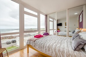 A bedroom with a large window, a bed with pillows, a flat-screen TV, and a view of the sea. - 2 Bed in Newquay (oc-p00214) (Newquay)