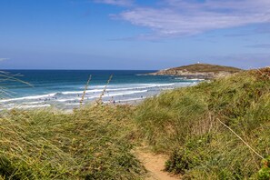 A coastal path leading to a beach with waves, grassy terrain, and a distant hill. - 2 Bed in Newquay (oc-p00214) (Newquay)