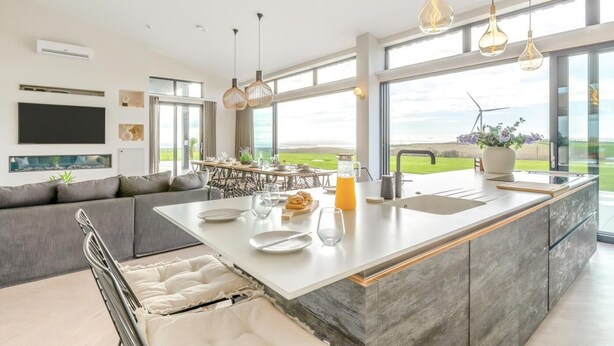 A modern kitchen with a large island, dining area, and a view of the outdoors. - 7 Bed in Marwood (oc-w32673) (Marwood)