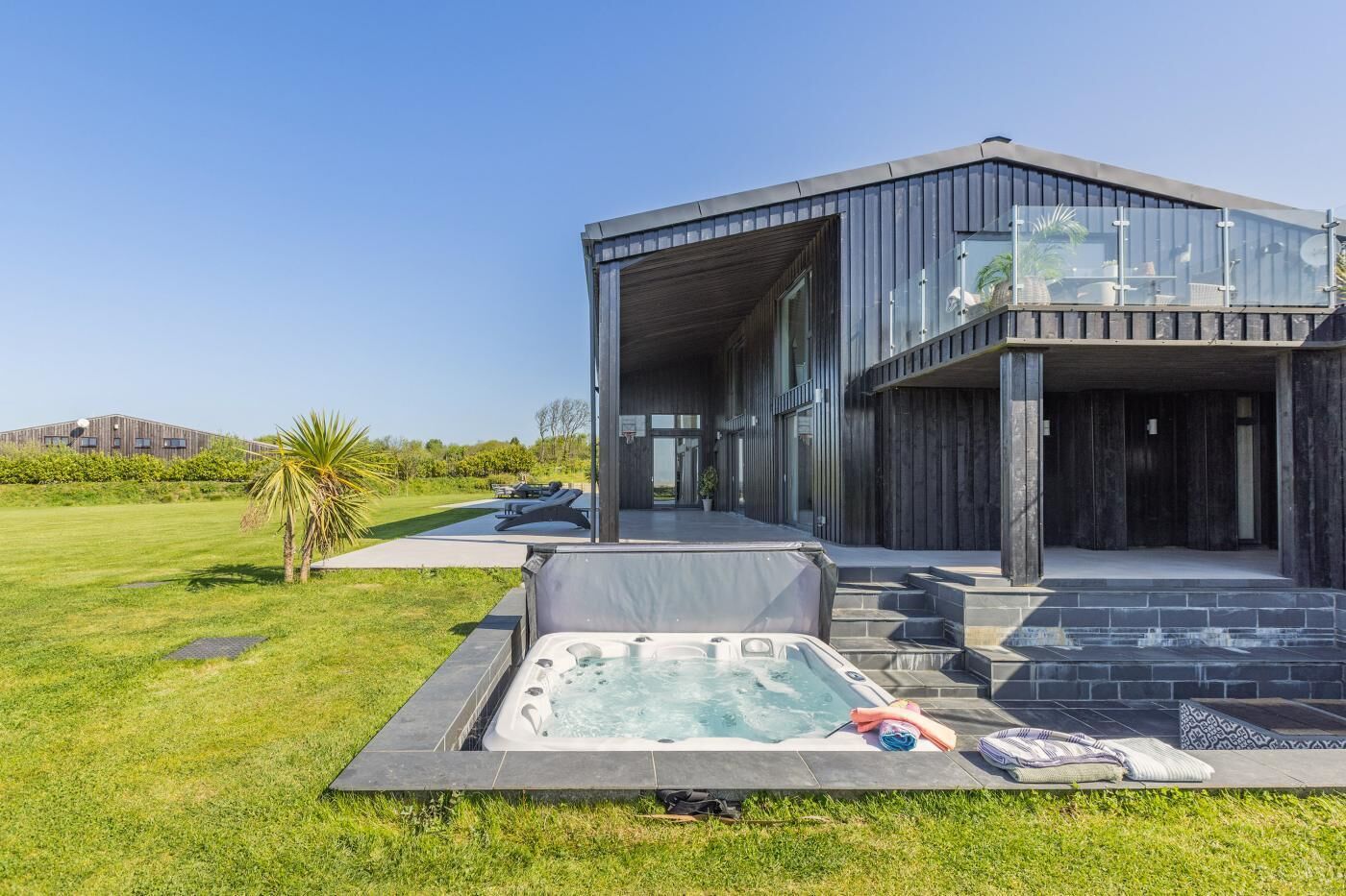 Ein modernes Haus mit Whirlpool, einer überdachten Terrasse und Blick auf eine Rasenfläche.