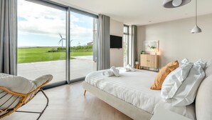 A modern hotel room with a large bed, a chair, a desk, and a view of wind turbines. - 7 Bed in Marwood (oc-w32673) (Marwood)