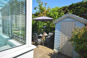 A patio with a table and chairs, a small shed labeled 'BEACH', and a window with blinds. - 2 Bed in Padstow (oc-p00337) (Padstow)