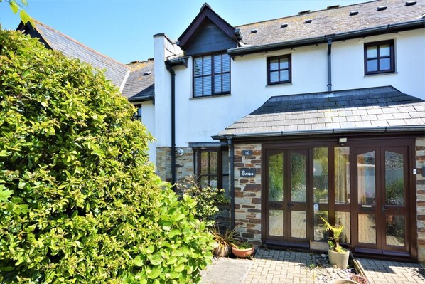 A white building with a stone facade, a sign reading "Sande," and a large glass door. - 2 Bed in Padstow (oc-p00337) (Padstow)