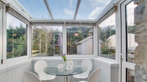 Een oranjerie met een glazen tafel en stoelen, omgeven door witte muren en stenen details.