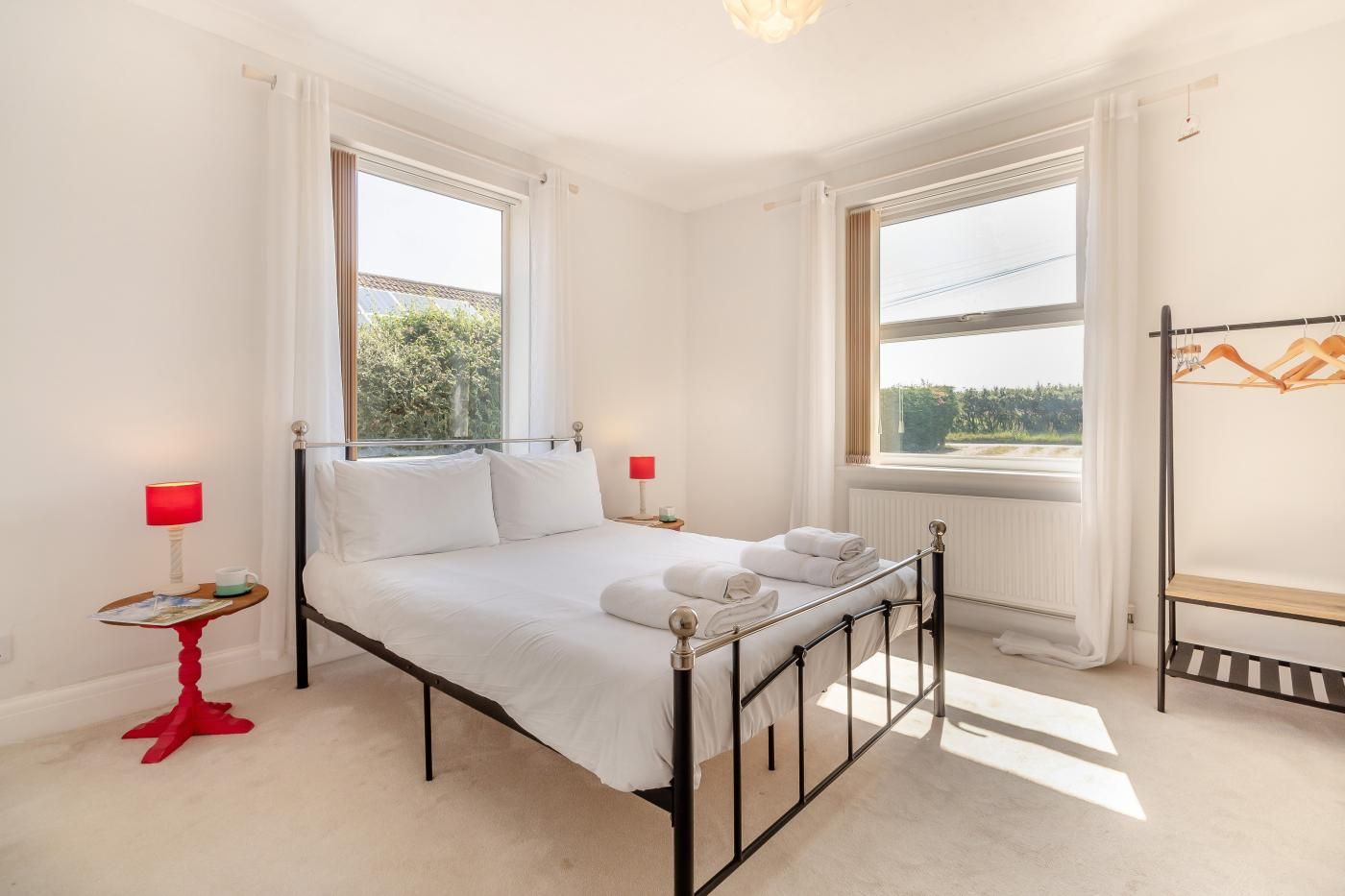 A bedroom with a bed, two bedside tables, a radiator, and a window with curtains.