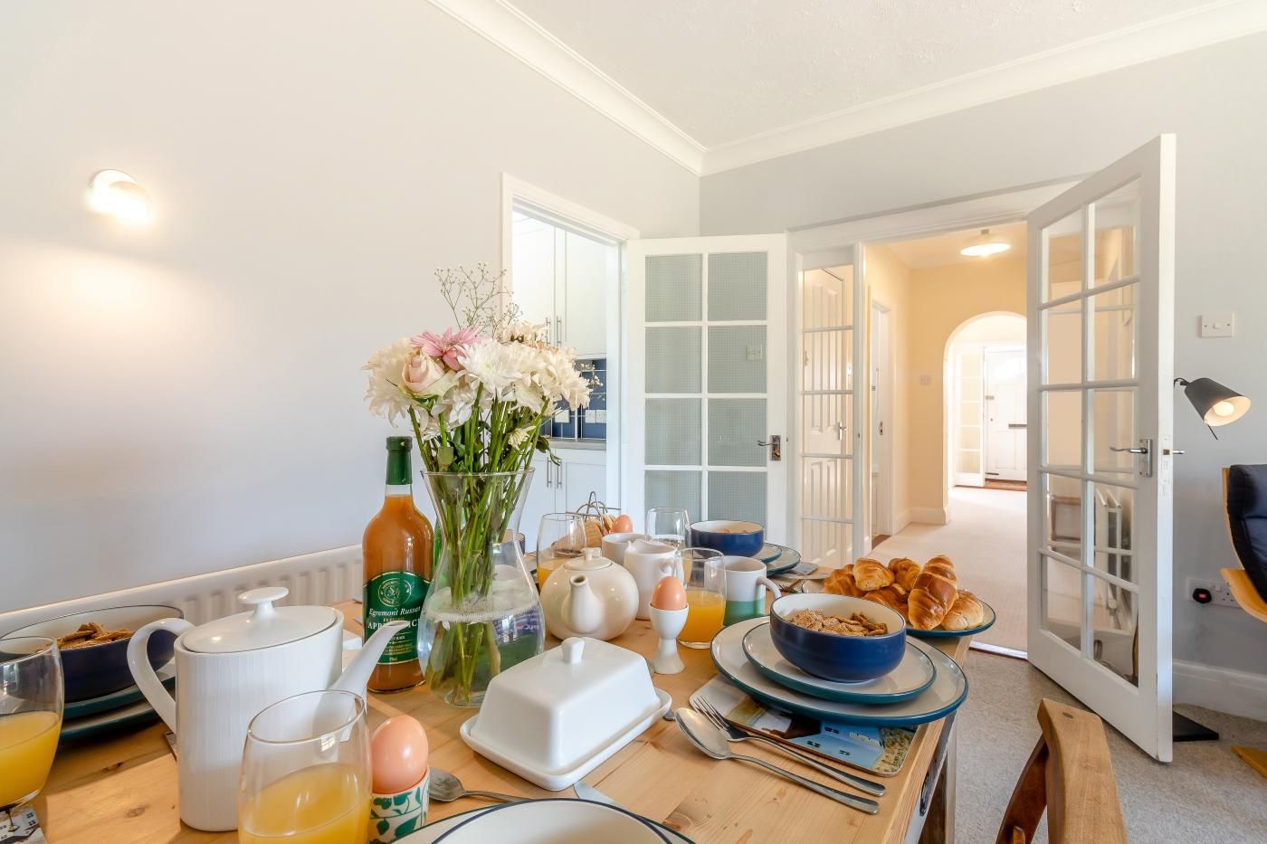 Et morgenbord dækket til to personer, med tallerkener, glas, en vase med blomster og forskellige spisemuligheder.