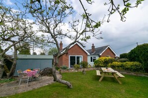 Une maison à deux étages, construite en briques, avec une porte d’entrée, un garage et un petit jardin agrémenté d’une table de pique-nique et de chaises.