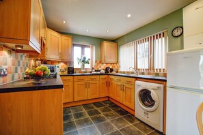 Une cuisine moderne avec des meubles en bois, un lave-linge encastré et une horloge au mur.