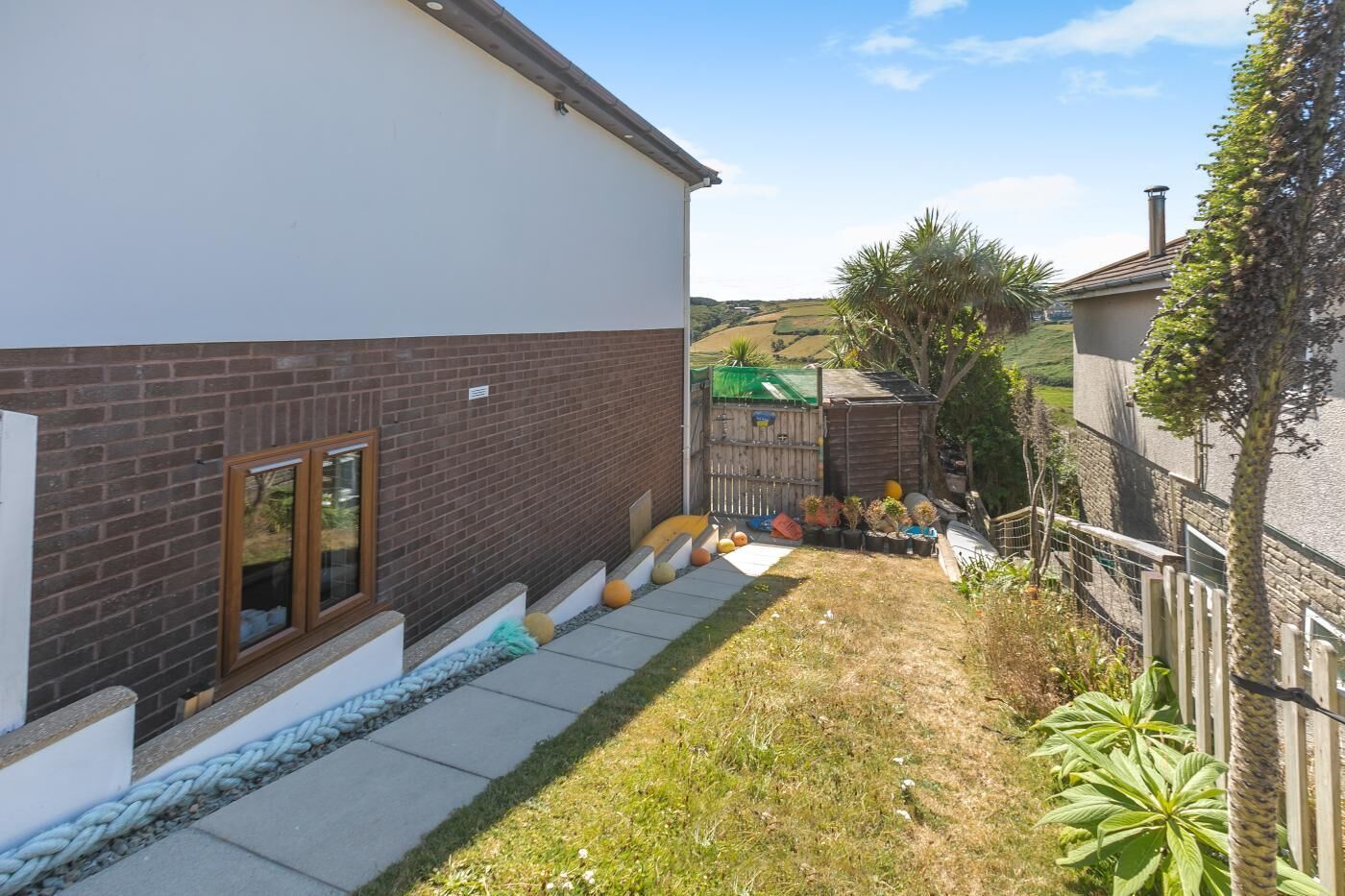 A residential property with a paved driveway, a brick wall, and a fenced garden area.