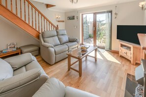 A spacious living room with a wooden staircase, a sofa set, a coffee table, and a television. - 2 Bed in Newquay (oc-p00335) (Mawgan Porth)