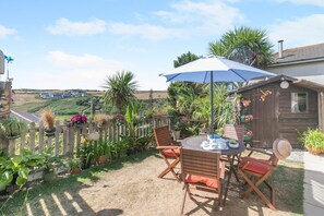 An outdoor patio with a table and chairs, surrounded by potted plants and a wooden fence. - 2 Bed in Newquay (oc-p00335) (Mawgan Porth)