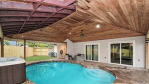 An outdoor swimming pool with a hot tub, stone flooring, wooden ceiling, and a covered patio area. - 4 BR Luxury Home in Friendswood (Friendswood)