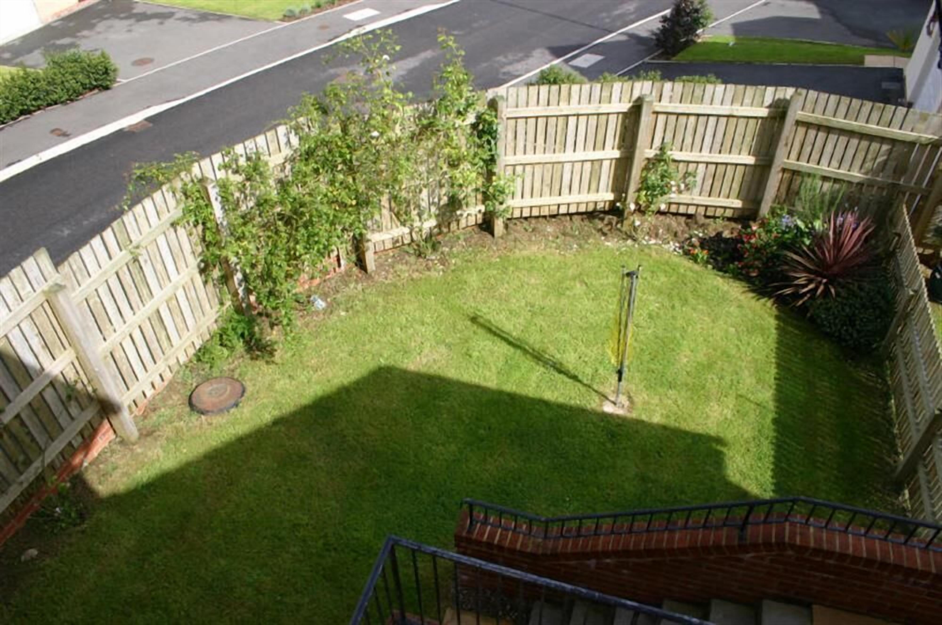 A fenced backyard with a grassy lawn, a wooden deck, and a metal fence.
