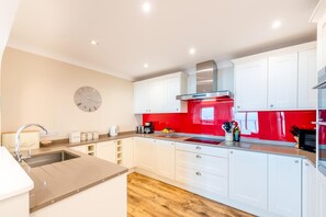 Une cuisine moderne avec des armoires blanches, un pare-feu rouge, une hotte de cuisinière en acier inoxydable et un plancher en bois.