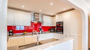 A modern kitchen with white cabinets, a red backsplash, stainless steel appliances, and a large island with a sink.