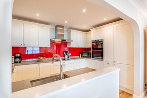 A modern kitchen with white cabinets, a red backsplash, stainless steel appliances, and a large island with a sink.