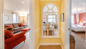 A hallway with a dining area, a living room with a sofa and ottoman, and a bedroom with a bed.