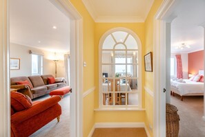 A hallway with a dining area, a living room with a sofa and ottoman, and a bedroom with a bed.