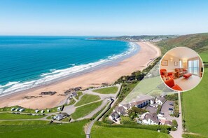 An aerial view of a coastal area with a beach, green fields, and residential buildings.