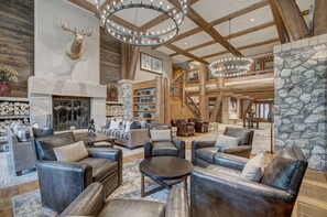 A spacious lobby with leather sofas, a stone fireplace, wooden beams, and a staircase leading to an upper level. - Spacious Condo with ski-in access | Hot Tub access (Avon)