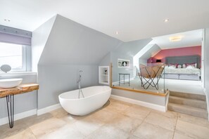 Un baño moderno con una bañera independiente, un tocador de madera y un amplio ventanal.