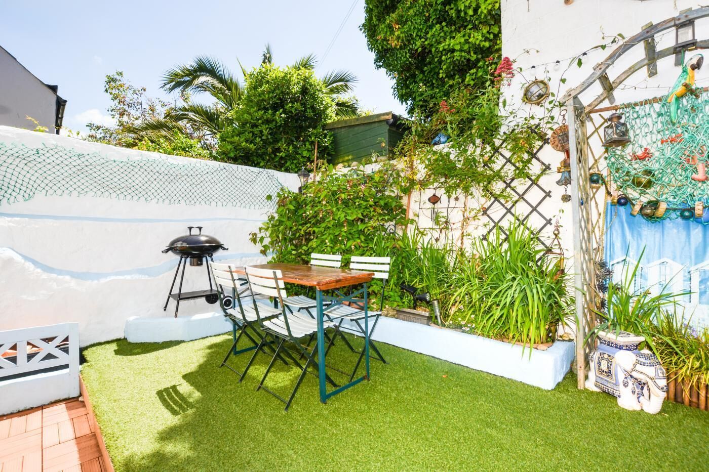 Eine Terrasse mit künstlichem Rasen, einem Grill und einem Tisch mit Stühlen.