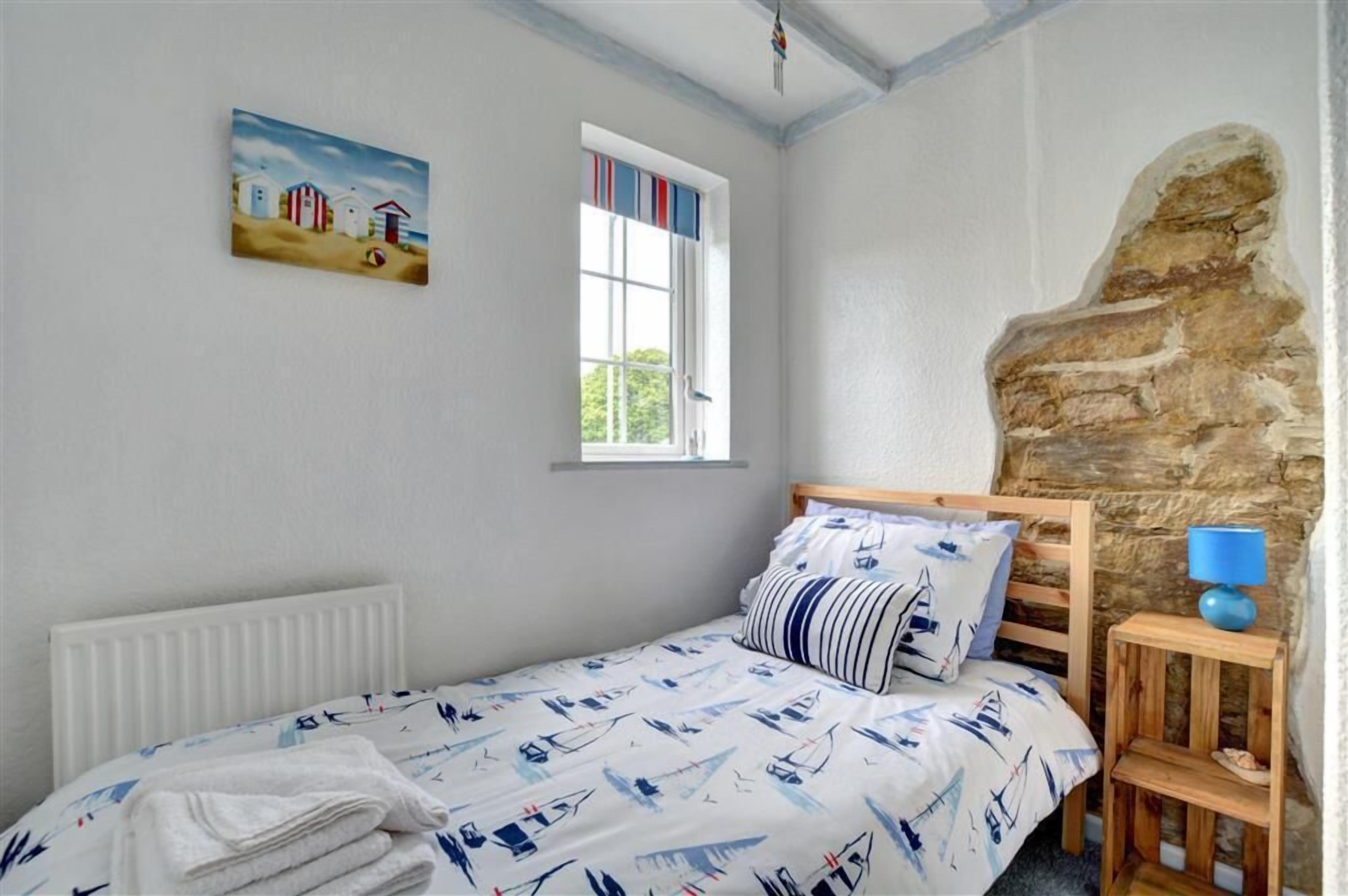A bedroom with a bed, a window, a painting, and a stone wall.