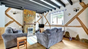 Een gezellige woonkamer met twee gestreepte banken, een houten salontafel en een stenen open haard.