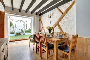 A dining area with a wooden table set for four, surrounded by wooden chairs with black cushions. A white textured wall and a wooden ceiling beam are visible. - 3 Bed in Newquay (oc-p00484) (Newquay)