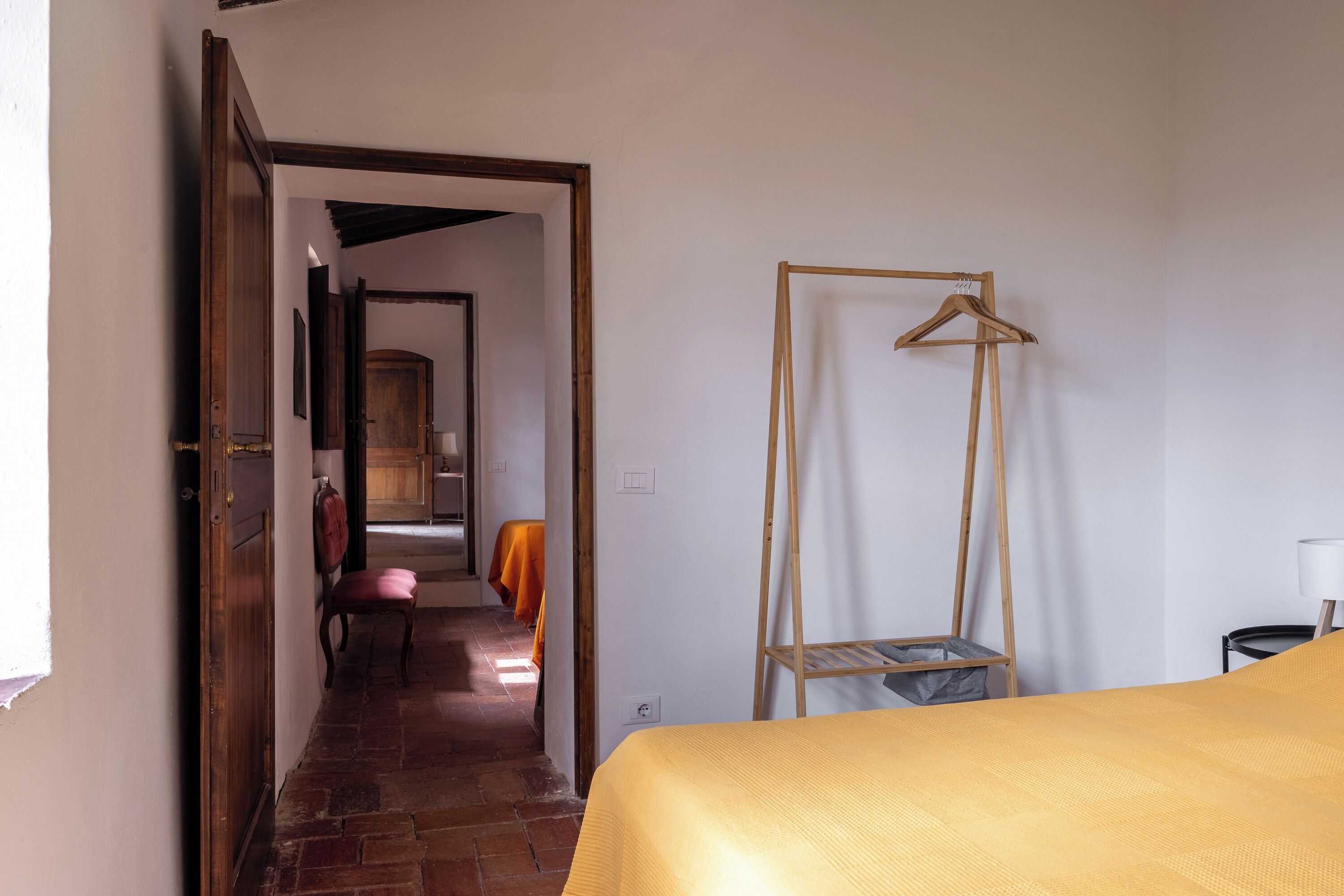 Een kamer met een bed, een houten kleerhanger, een stoel en een tafel.