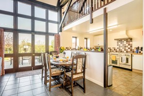 A dining area with a table set for four, a kitchen with modern appliances, and a view through large windows. - 3 Bed in Little Ellingham (oc-2147) (Little Ellingham)