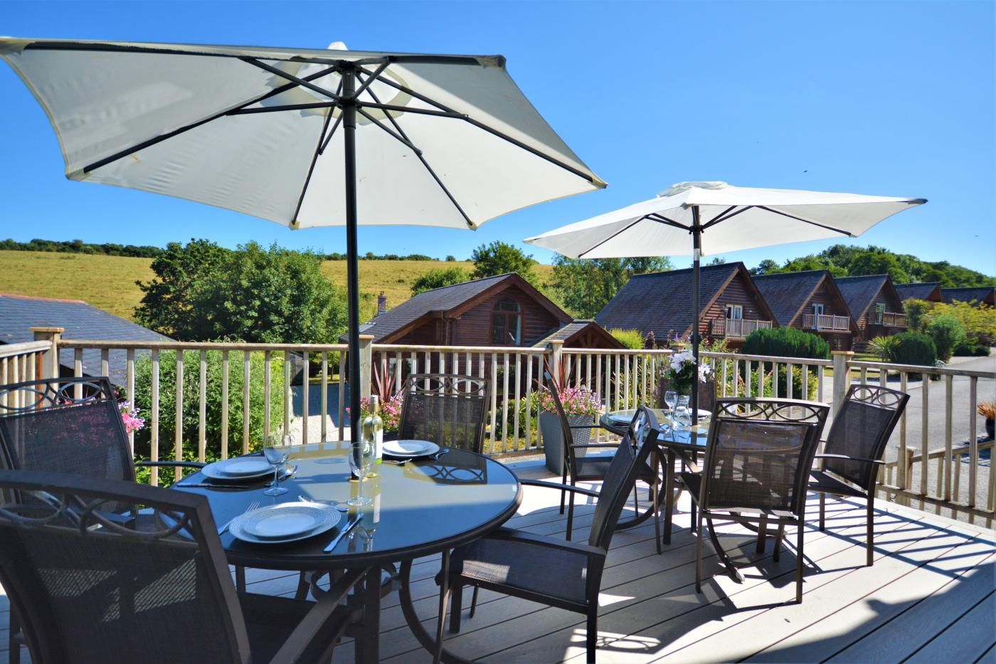 A deck with outdoor seating, including tables and chairs, and two large umbrellas providing shade.
