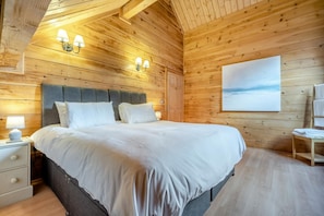 Un dormitorio de cabaña de madera con una cama grande, dos lámparas de noche, una mesita de noche y un cuadro en la pared.