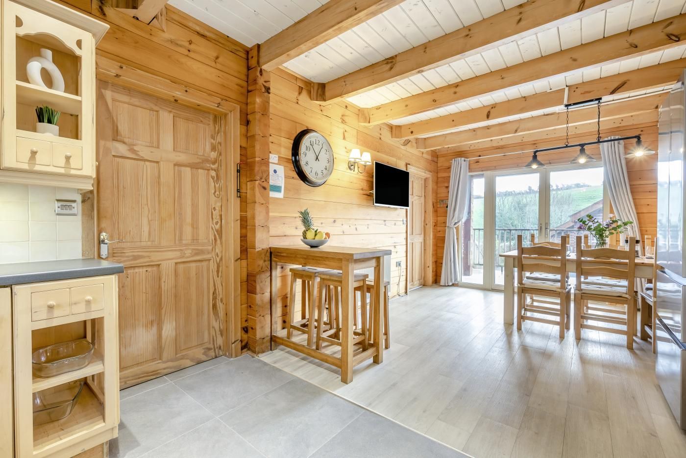 A wooden interior with a kitchen area, dining space, and a large window providing a view of the outdoors.