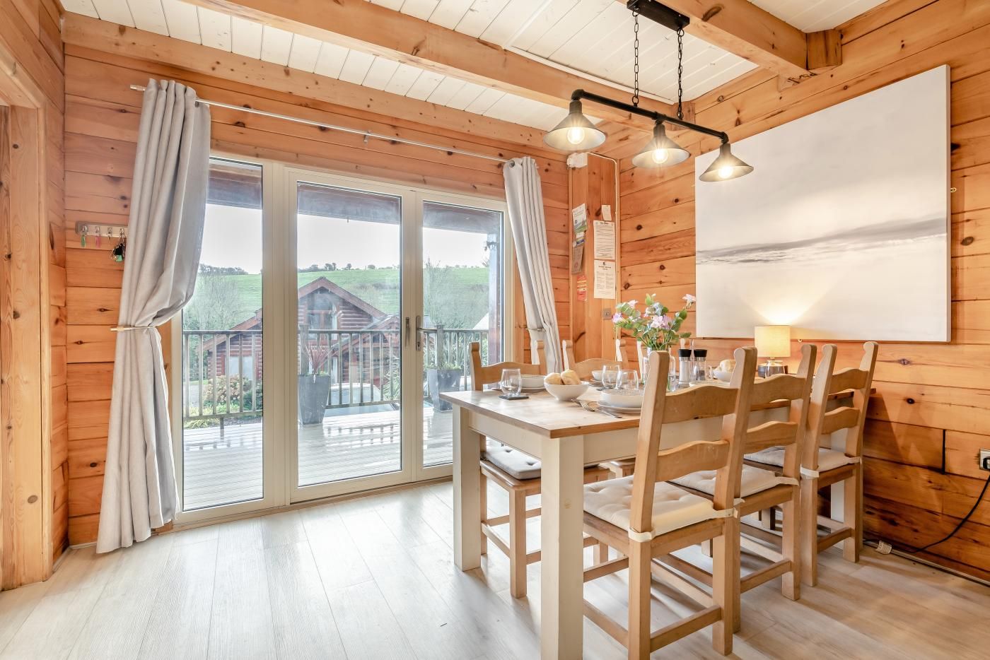 A wooden cabin with a dining area, a balcony with a view, and a large window.