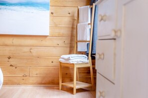 Interior de una cabaña de madera con una silla de madera, un perchero y vistas al océano a través de una ventana.