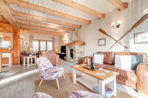 A cozy living room with wooden beams, a stone fireplace, leather sofas, and a marble-patterned armchair. - 3 Bed in Wadebridge (oc-p00104) (Little Petherick)