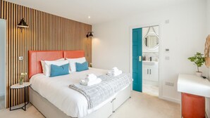 A modern hotel room with a large bed, a wooden slat wall, a bathroom with a blue door, and a white vanity. - 2 Bed in Newburgh (oc-f32595) (Newburgh)