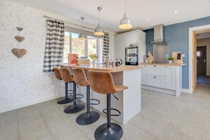 A modern kitchen with a central island, bar stools, pendant lights, and a view of the outdoors.