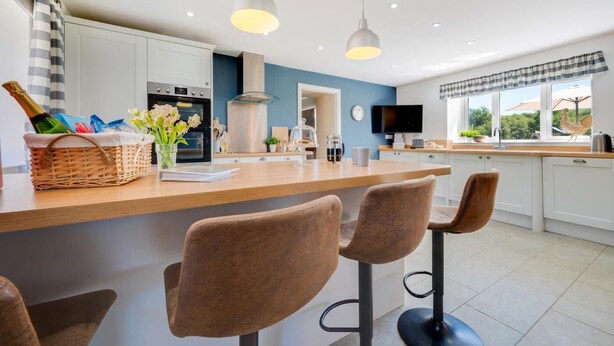 A modern kitchen with a central island, bar stools, pendant lights, and a view of the outdoors. - 4 Bed in Welshpool (oc-wab267) (Welshpool)