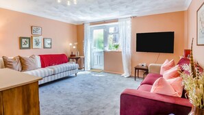 A living room with a sofa, a red armchair, a TV, and a window with curtains. - 2 Bed in Cromer (oc-t32572) (Cromer)