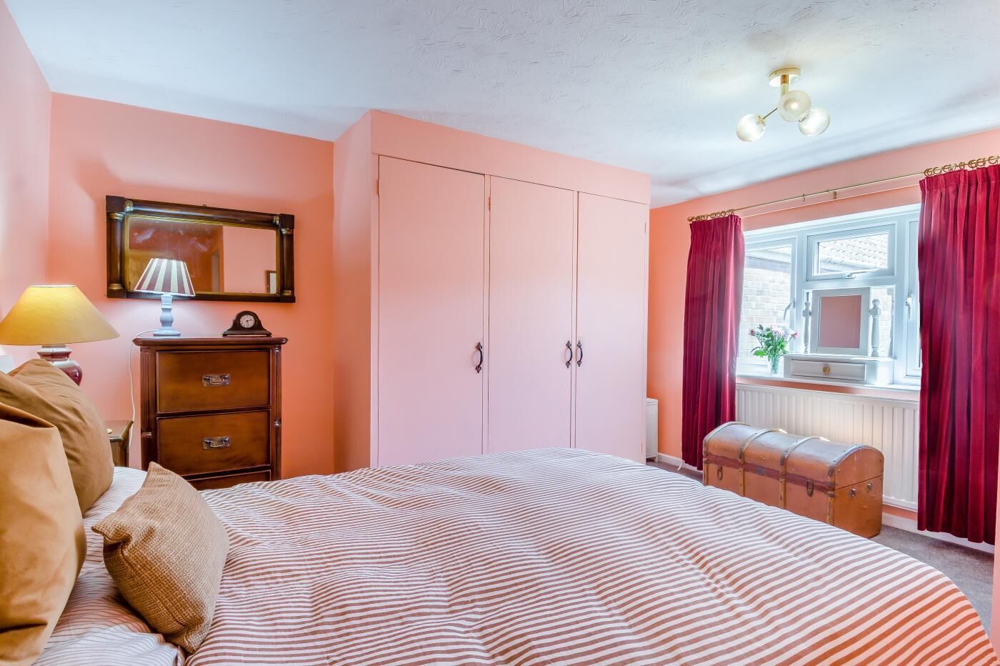 Une chambre à coucher comprenant un lit, une commode, une armoire, une fenêtre avec des rideaux et une lampe.