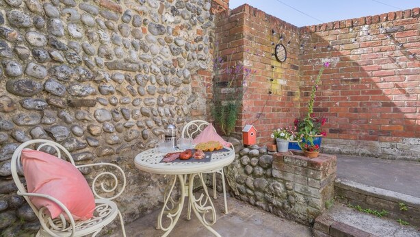 A stone wall, a brick wall, a round table with food, two chairs, and a small birdhouse. - 2 Bed in Cromer (oc-t32572) (Cromer)