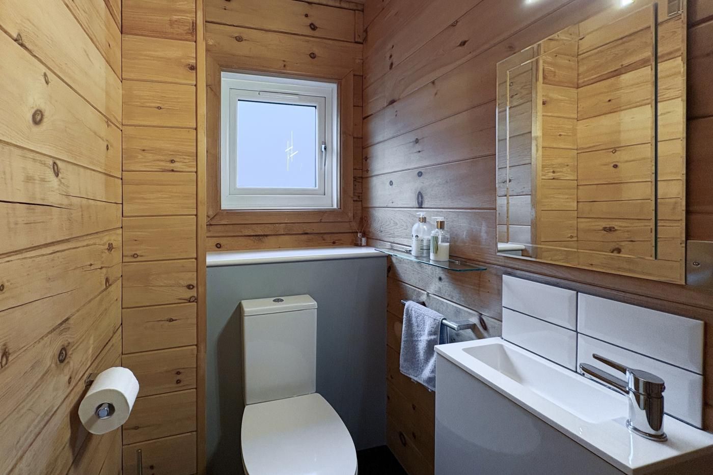 Une salle de bain aux murs lambrissés, équipée de toilettes, d’un lavabo et d’un miroir.