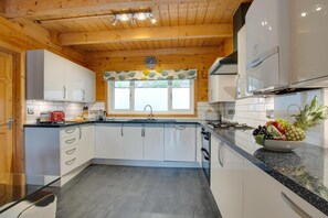 A modern kitchen with wooden beams, white cabinetry, a large window, and a fruit bowl on the counter.